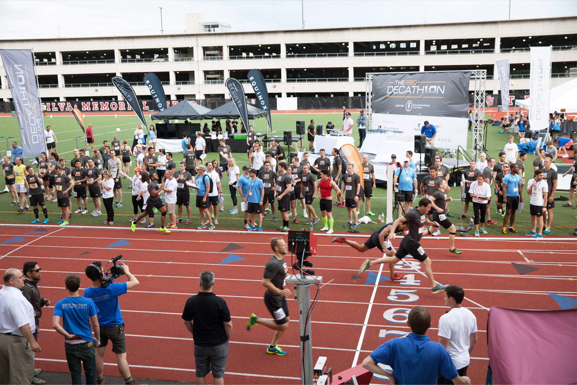 D10 athletes sprint lanes 4 through 6 on a red track at the RBC Decathlon while teammates watch from the infield.